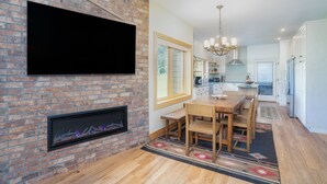 A modern kitchen with a brick wall, a flat-screen TV, a fireplace, and a dining area with wooden furniture.