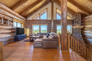 A log cabin interior with a large wooden ceiling, stone fireplace, and a sectional sofa. - Adams Rest 3 Bedroom Cabin (The Dalles)