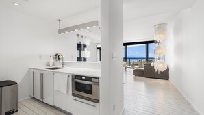 Una cocina moderna con electrodomésticos de acero inoxidable, una isla grande y vista al océano desde la sala.