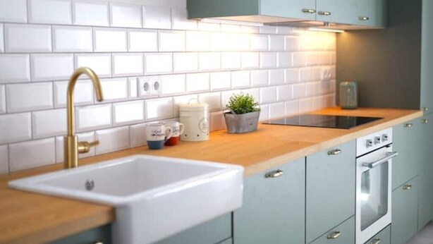 A kitchen with white subway tiles, a gold faucet, a sink, a stove, and cabinets.