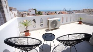 A rooftop terrace with two black wire chairs, a small table, and a potted plant.