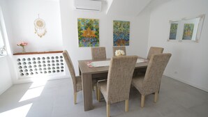 A dining area with a wooden table and six chairs, a dreamcatcher, and two paintings on the wall.
