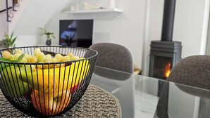 A modern living room with a glass table, a black wire fruit bowl, a fireplace, and a TV on a white shelf. - Little House of Heaven (Cortes do Meio)