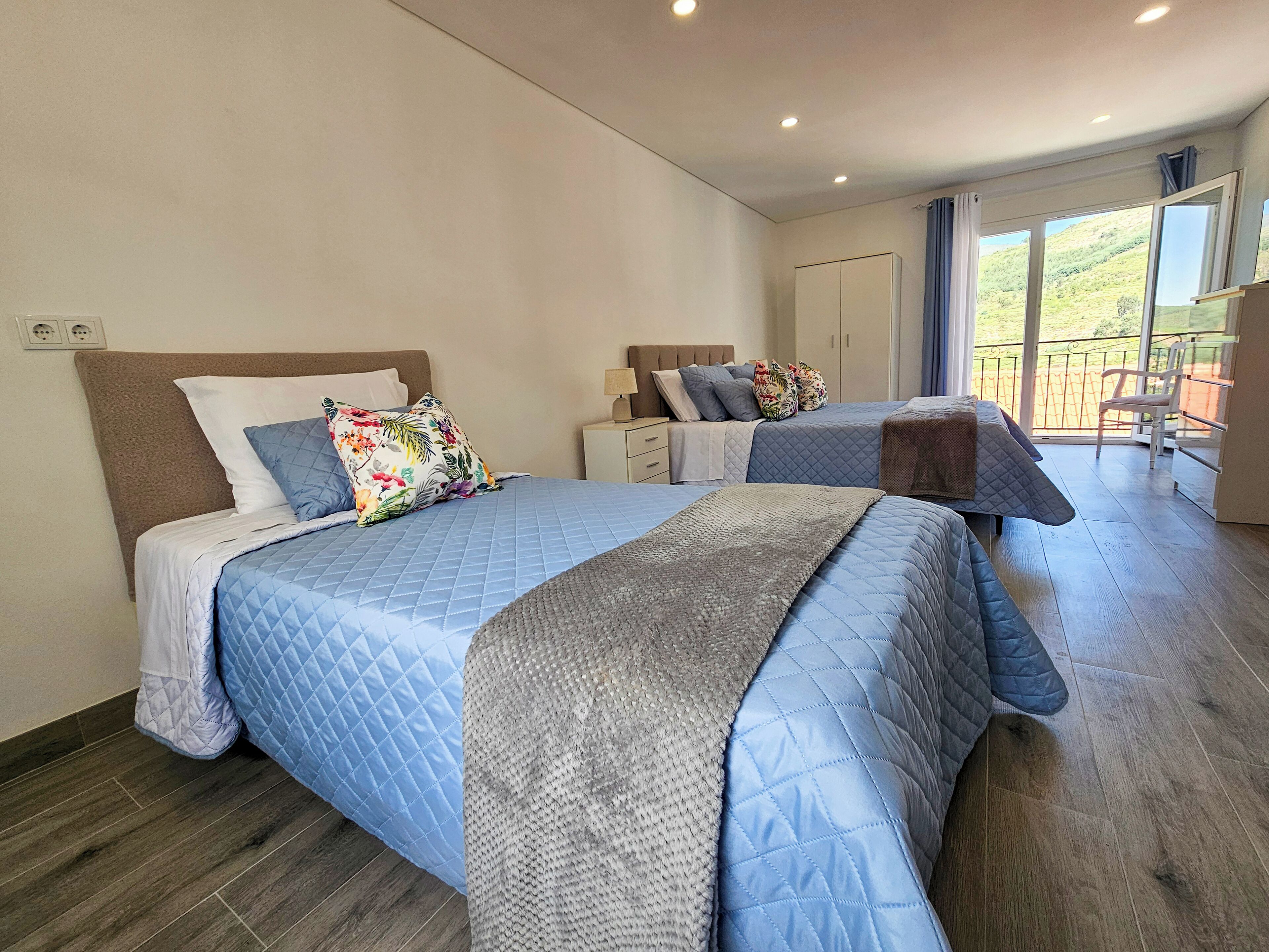 Een slaapkamer met twee bedden, een balkon en uitzicht op de omgeving.