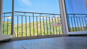 A balcony with a metal railing, a white chair, and a view of a green hillside. - Little House of Heaven (Cortes do Meio)
