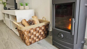 A modern living room with a wood-burning stove, a white entertainment unit, and a woven basket filled with firewood. - Little House of Heaven (Cortes do Meio)