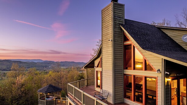 Una casa grande con terraza, chimenea y vistas a las montañas.