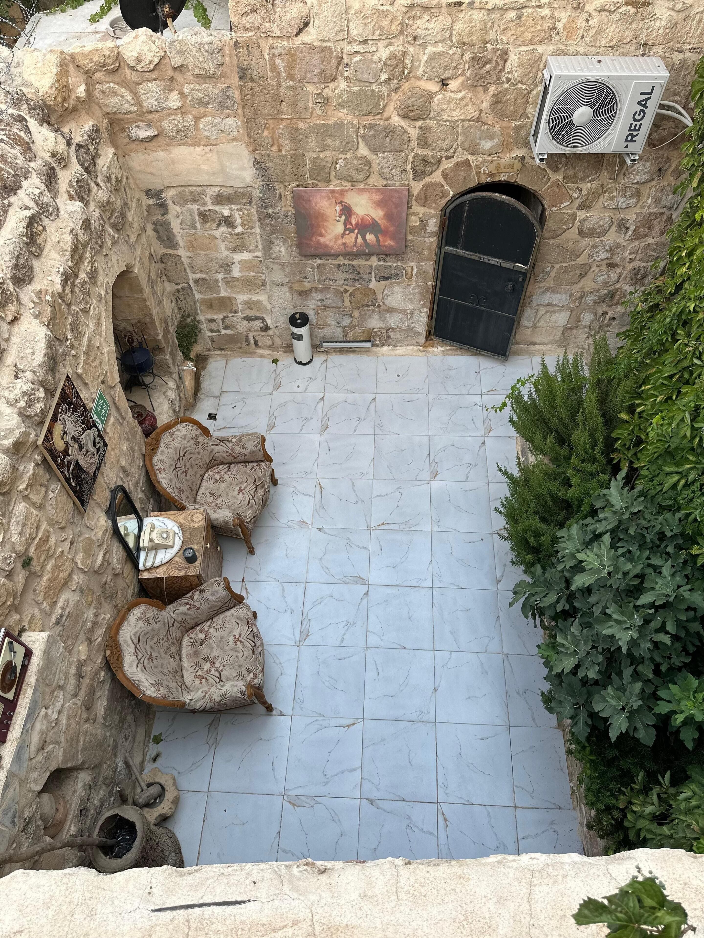 Pátio de pedra com piso de azulejos, uma porta preta e um aparelho de ar condicionado fixado na parede.