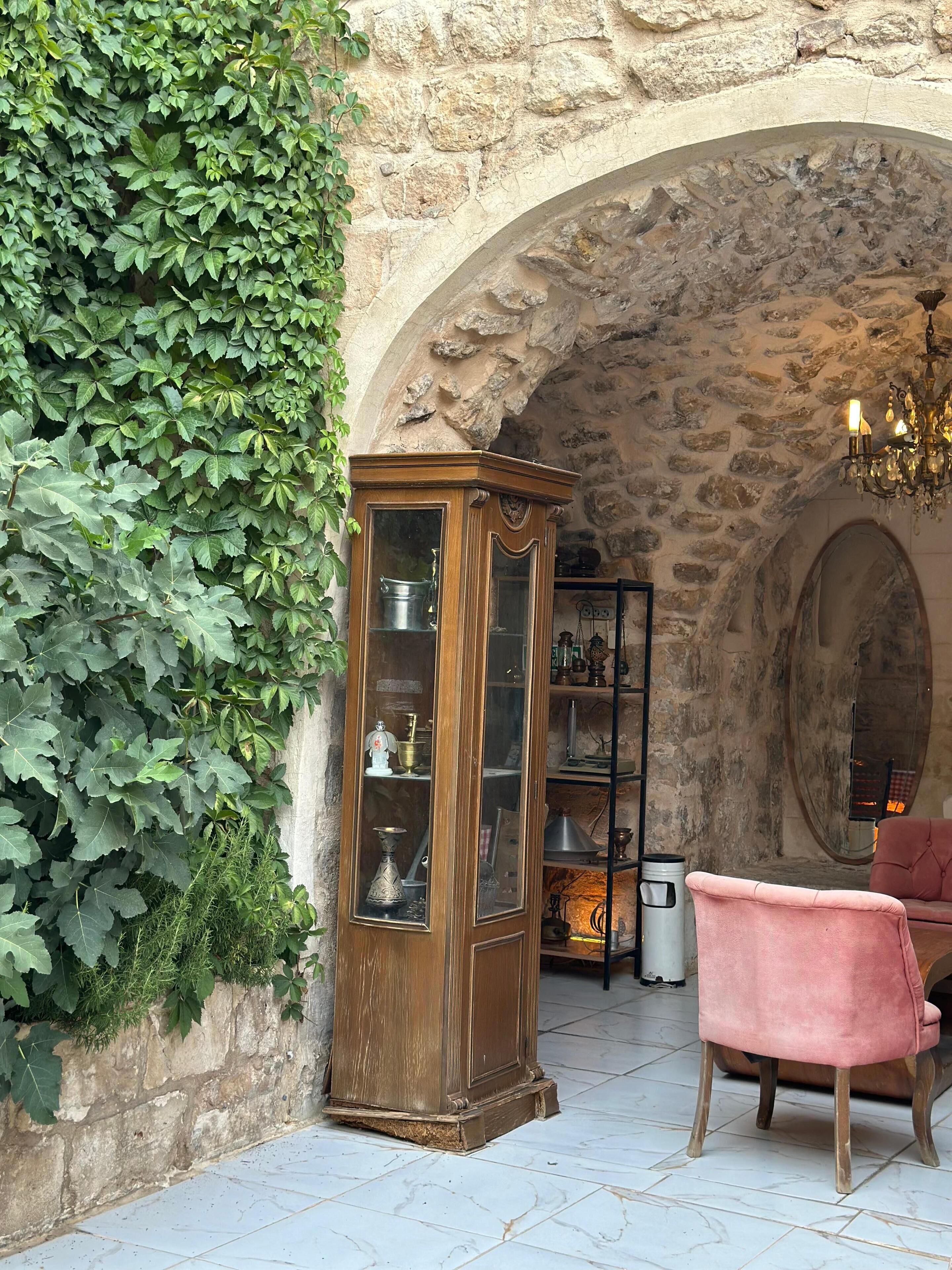 A stone-walled room with a wooden cabinet, a pink chair, and a chandelier.