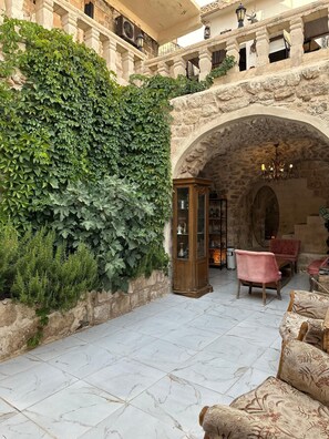 A courtyard with a stone wall covered in greenery, a wooden cabinet, and a seating area with patterned cushions. - ACABEY KONAĞI (Mardin)