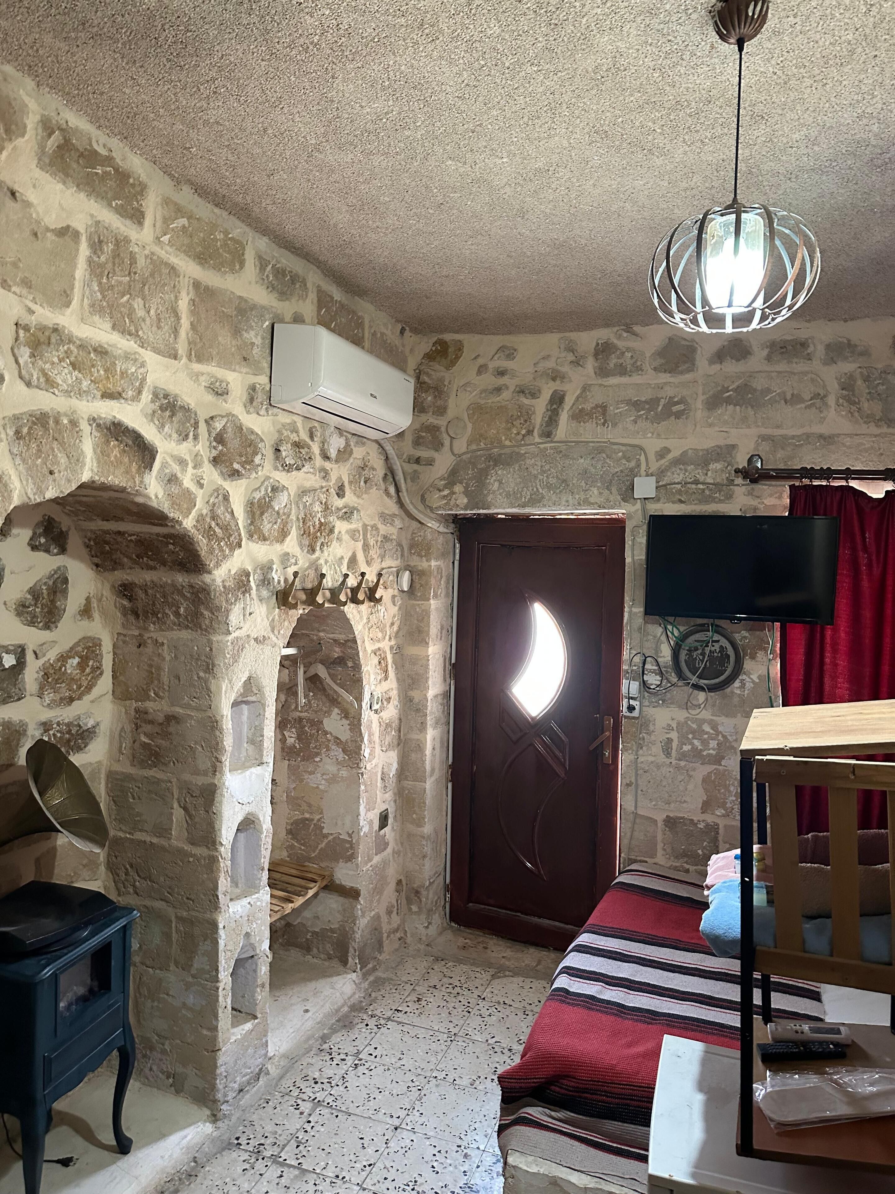 Une pièce rustique aux murs de pierre, avec une porte en bois, une petite table, une chaise et un téléviseur fixé au mur.