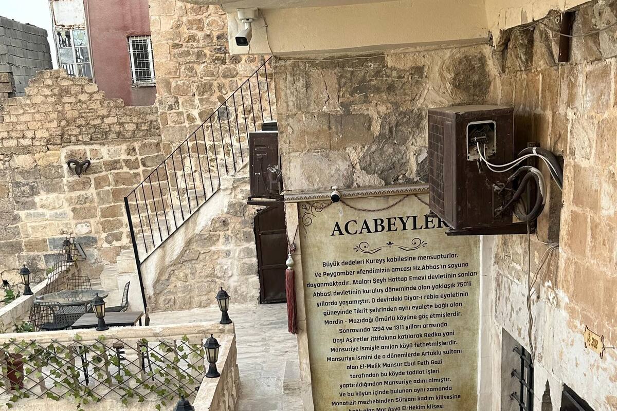 A courtyard with stone walls, a small table with chairs, and a signboard.