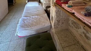 A stone-walled room with two beds, a bench, and a small seating area. - ACABEY KONAĞI (Mardin)