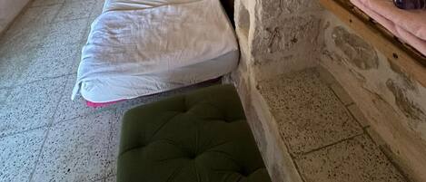 Una habitación con paredes de piedra, dos camas, un banco y un pequeño rincón de descanso.