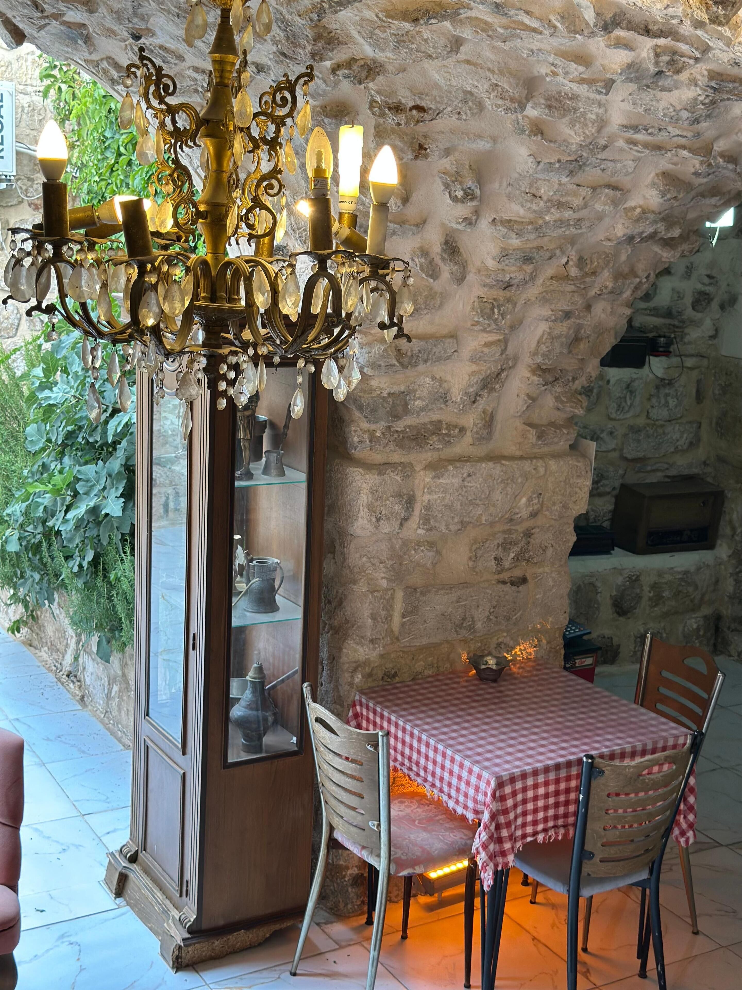 Interior de paredes de piedra con un candelabro, una mesa con mantel a cuadros y sillas.
