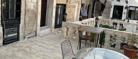 An outdoor patio with stone flooring, a round glass table, and metal chairs.