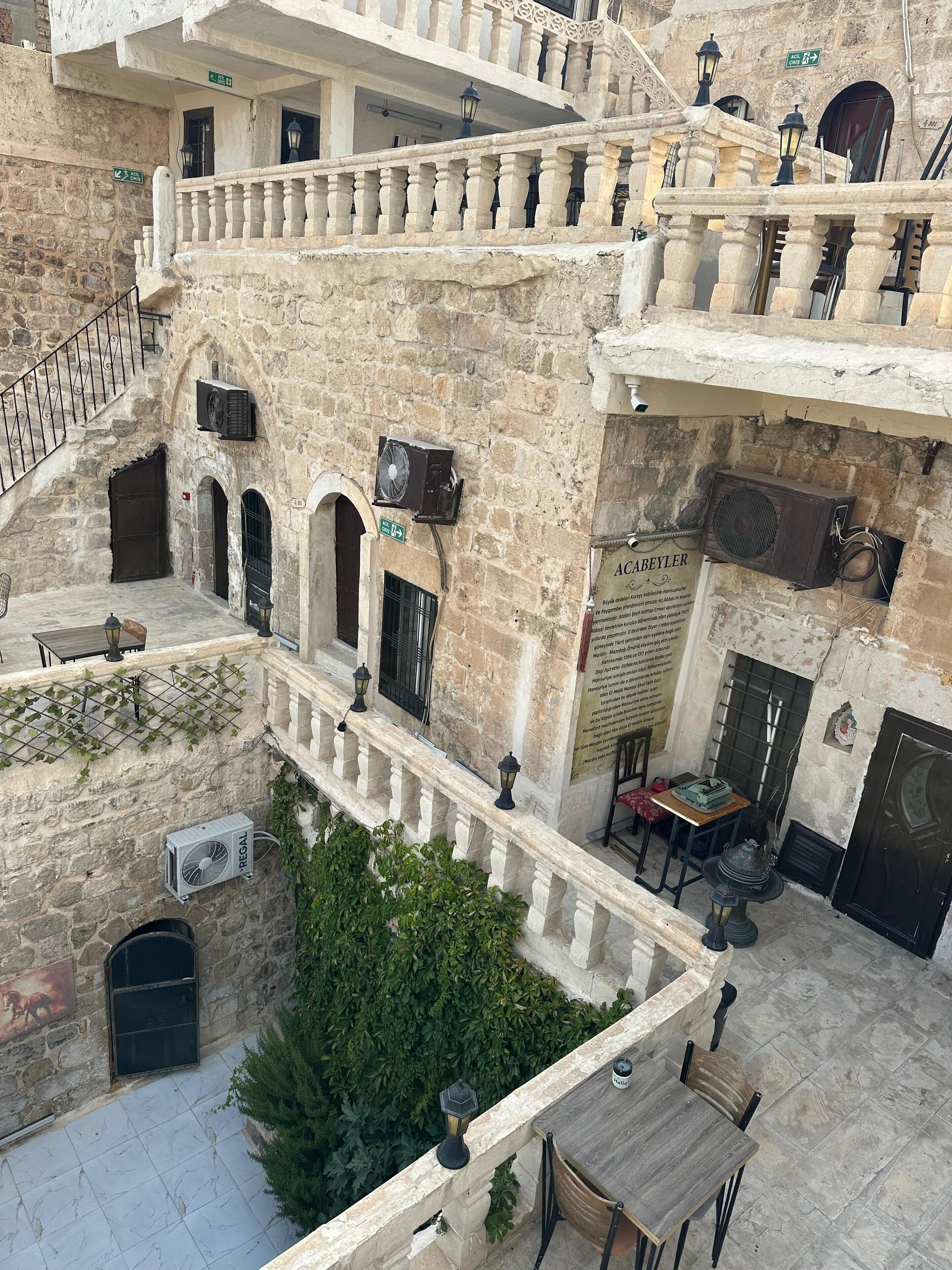 Un bâtiment en pierre à plusieurs niveaux, doté de balcons, d’un espace extérieur aménagé pour s’asseoir et d’un escalier.