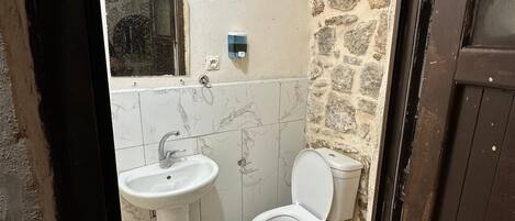 Un baño con piso de mármol, lavamanos blanco, inodoro y pared de piedra.