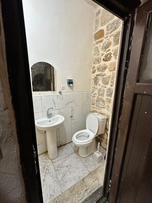 A bathroom with a marble floor, a white sink, a toilet, and a stone wall. - ACABEY KONAĞI (Mardin)