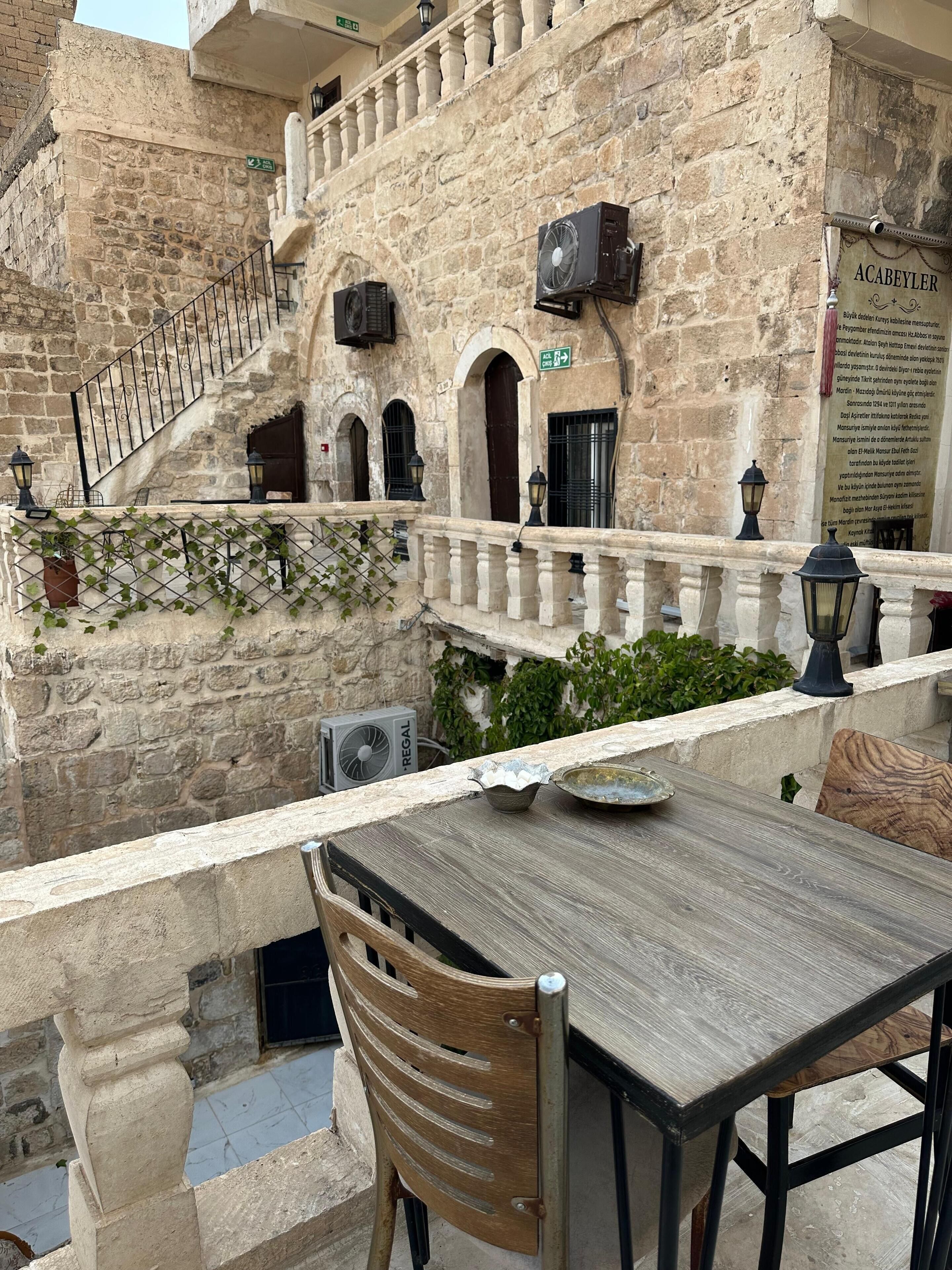 Un bâtiment en pierre doté d’un balcon, d’un espace extérieur aménagé pour s’asseoir et d’un escalier.