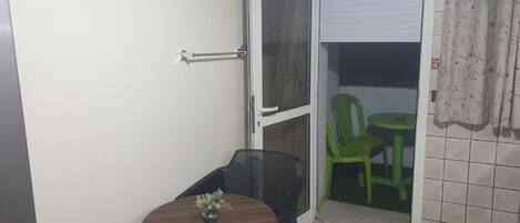 Un pequeño balcón con mesa y sillas, una puerta corrediza de vidrio y suelo de baldosas.