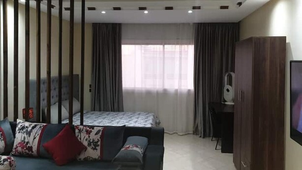 A modern hotel room with a bed, a sofa, a TV, and a wardrobe. - Superb studio at the ocean (Rabat)