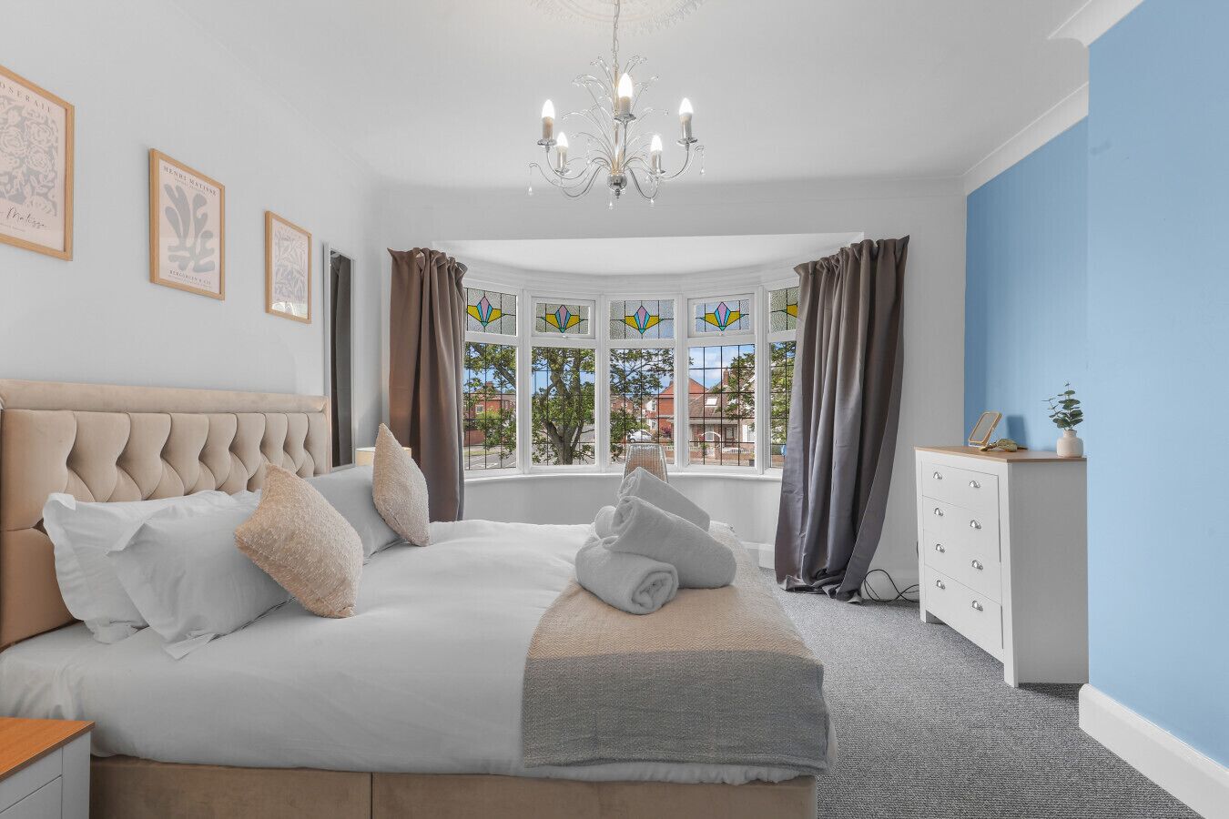 A bedroom with a large bed, a dresser, a chandelier, and a window with curtains.