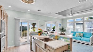 A modern kitchen with a large island, sliding glass doors to a balcony, and a bright, airy living area with a blue sofa.