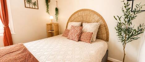 Une chambre à coucher comprenant un lit, une table de chevet, une lampe, une plante fixée au mur et une plante en pot.