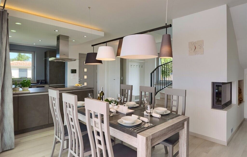A modern kitchen with a dining area, featuring a central island, pendant lighting, and a staircase.