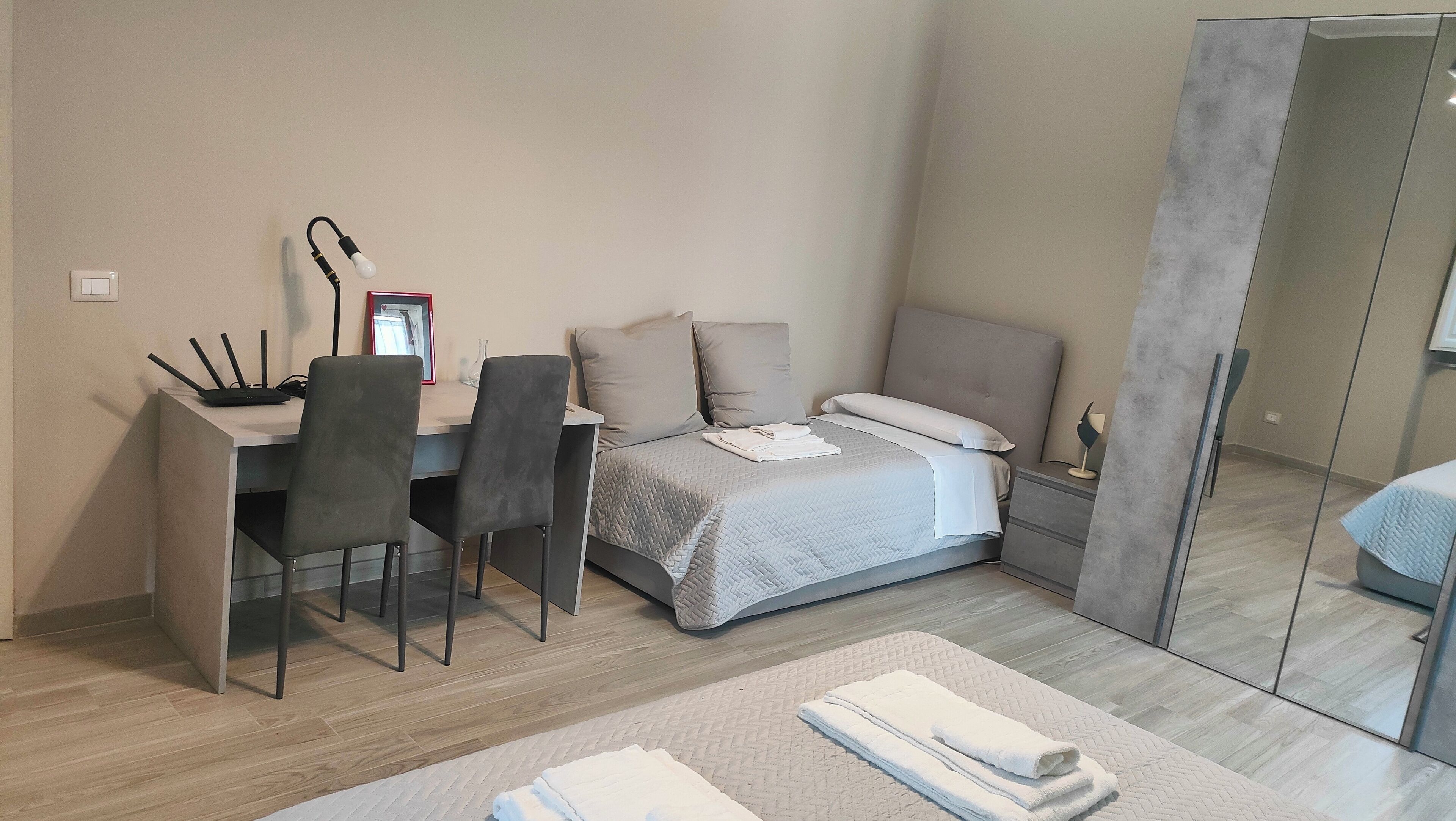 A bedroom with a bed, bedside table, lamp, and a desk with chairs.