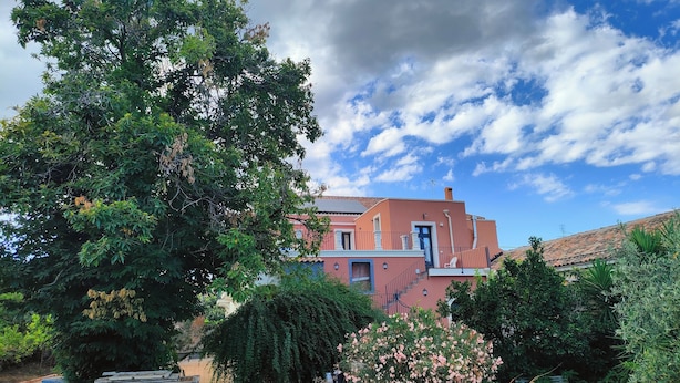 Una casa a due piani con facciata rossa, un balcone e un giardino ricco di piante e fiori.