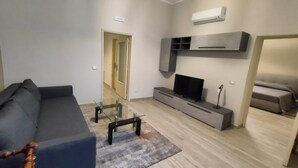 Un soggiorno moderno con un divano grigio, un tavolino in vetro, un televisore a schermo piatto su un mobile TV grigio e un divano in lontananza.