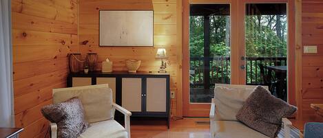 A wooden cabin interior with two beige armchairs, a small table, and a cabinet with decorative items.