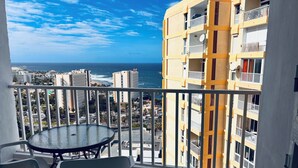 A balcony with a round table and two chairs, overlooking a cityscape and the ocean. - Troya Beach Apartments (Playa de la Américas)