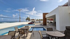 A poolside area with lounge chairs and tables, overlooking the ocean.