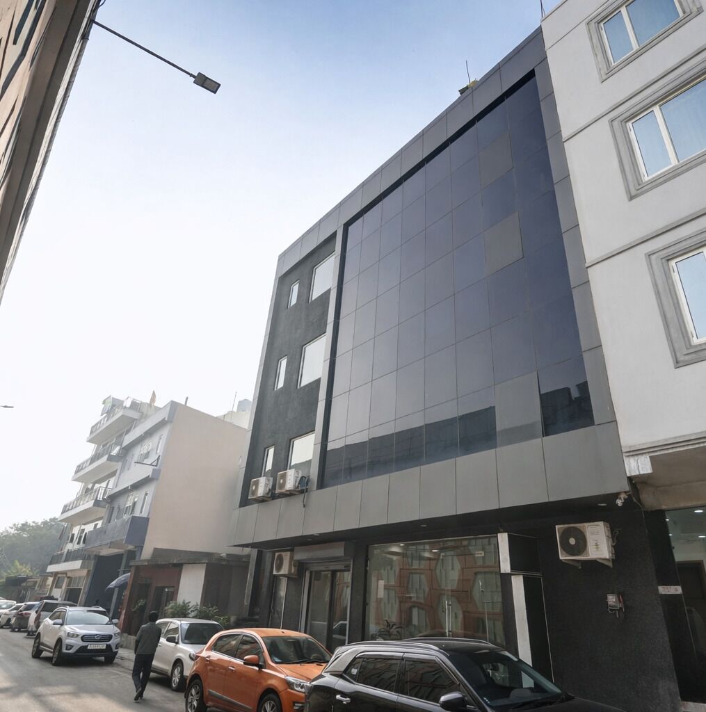 A modern building with a glass facade, parked cars, and a clear sky.