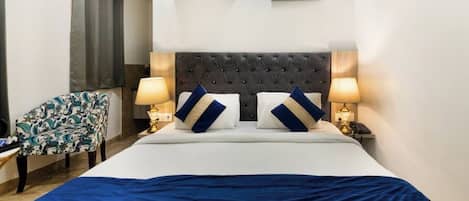 A hotel room with a large bed, two bedside lamps, a chair, an air conditioner, and a painting on the wall.