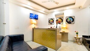 A reception area with a sofa, a reception desk, a TV, and framed pictures on the wall. - Hotel Evergreen Stay (New Delhi)