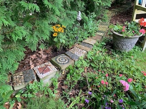 Un sendero en un jardín con losetas de piedra decorativas, rodeado de plantas y flores diversas.