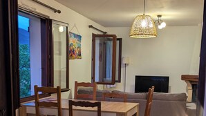 Un comedor con una mesa y sillas de madera, un sofá, un televisor y una lámpara colgante.