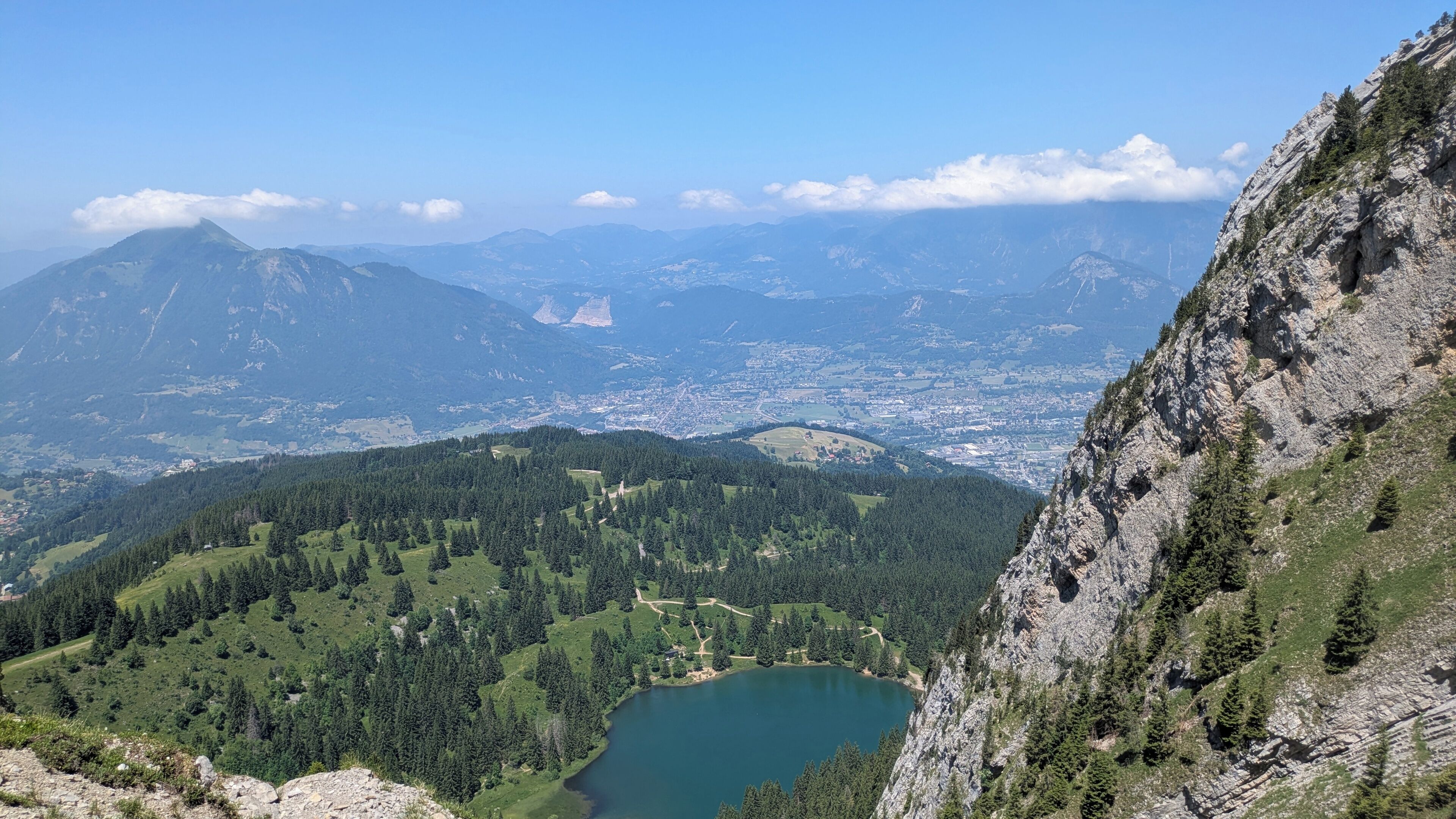 Un paysage montagneux avec un lac, des zones boisées et une ville située au loin.