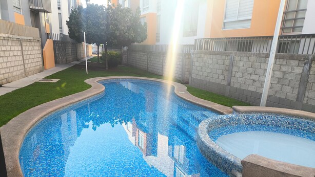 En swimmingpool med mosaikfliser, omgivet af en murstensmur og en græsplæne.