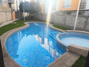 Une piscine aux carreaux de mosaïque, entourée d’un mur de briques et d’une pelouse.