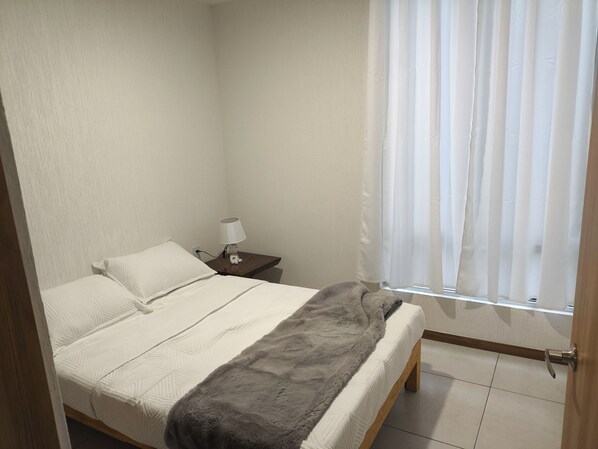 A neatly made bed with a fluffy blanket, a bedside lamp, and a nightstand with a small figurine.