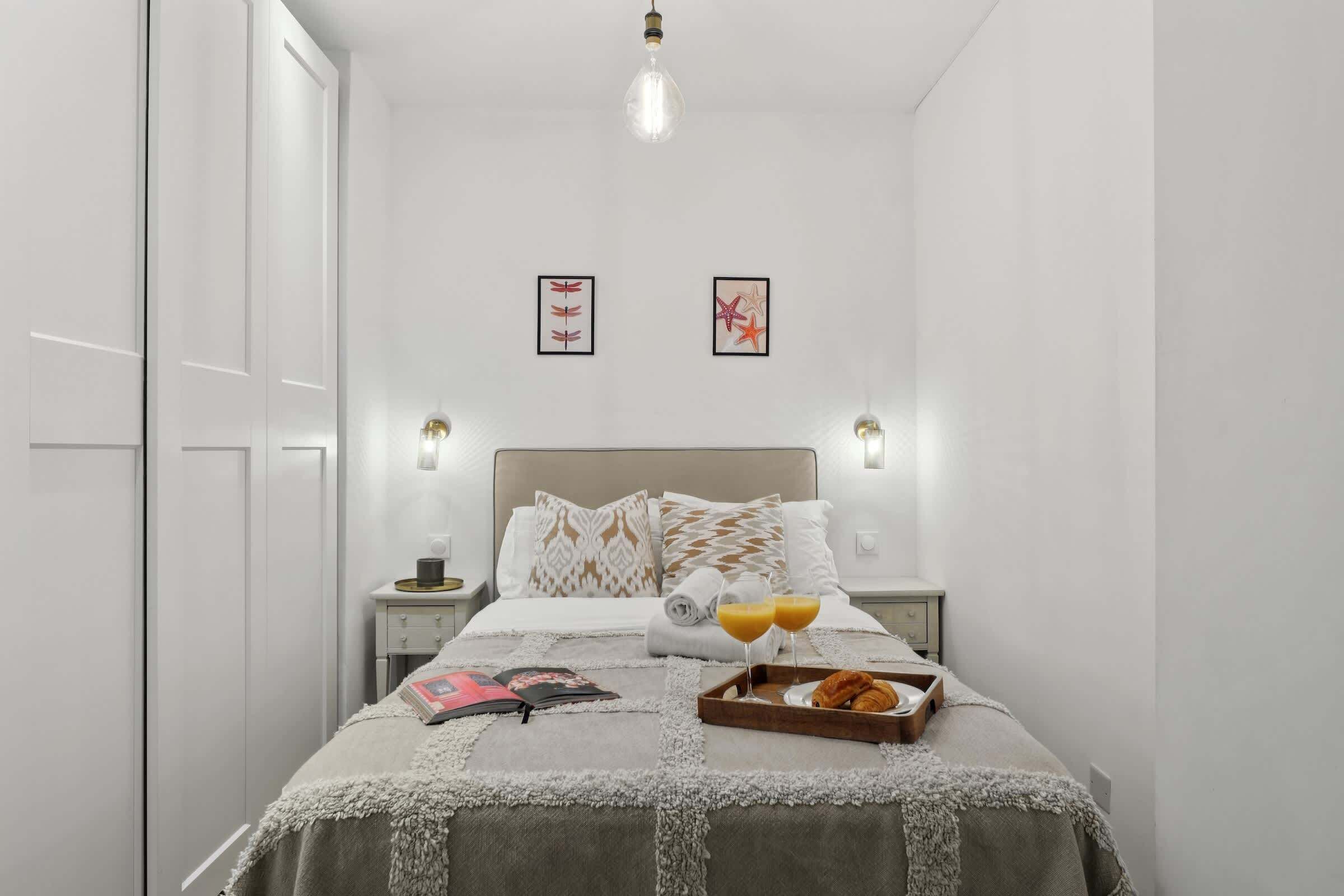 Une chambre à coucher bien rangée, avec un lit, des tables de chevet et un plateau contenant des croissants et du jus d’orange.
