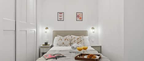 A neatly arranged bedroom with a bed, bedside tables, and a tray with croissants and orange juice.