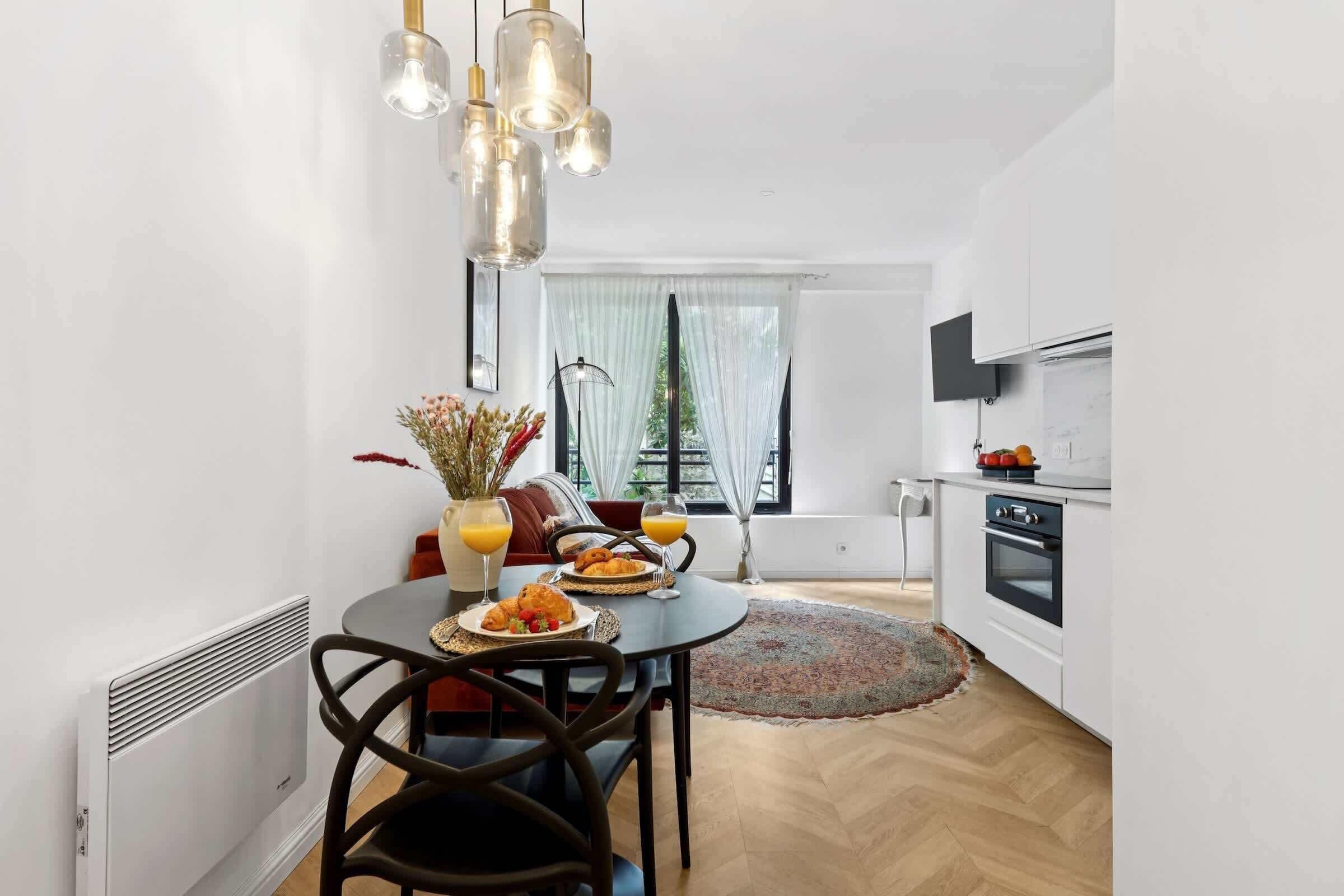 A modern kitchen with white cabinets, a built-in oven, and a dining area with a round table and chairs.