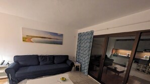 Un salon avec un canapé bleu foncé, une table basse blanche et une porte en verre donnant sur la cuisine.
