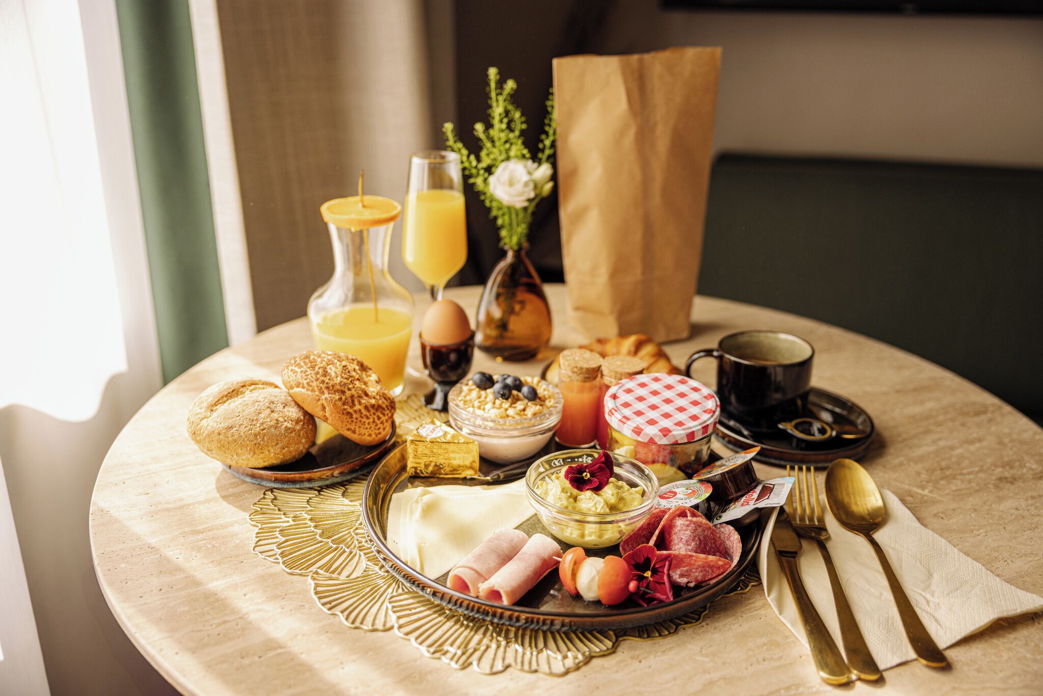 Un desayuno con una variedad de comidas y bebidas sobre una mesa redonda, incluyendo pasteles, huevos y una botella de jugo de naranja.